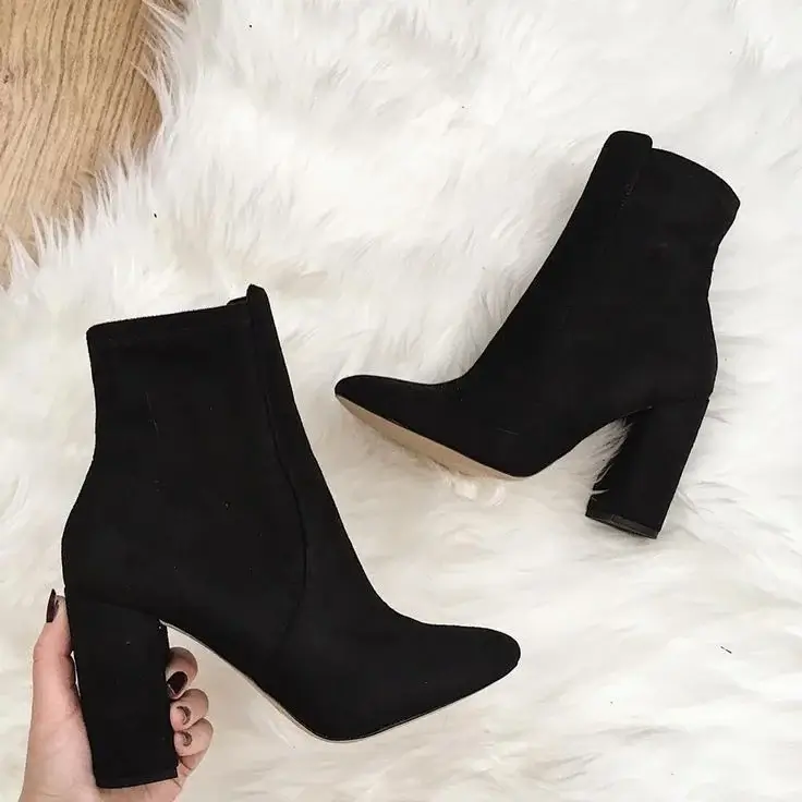 Black suede ankle boots with block heels displayed on a white fur background
